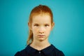 Portrait of serious seven year old girl with freckles and red hair on blue isolated background, expresses sincerity or