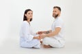 Portrait of serious sporty family of woman, man sitting with crossed legs on floor, holding hands on white background.