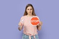 Serious strict bossy woman showing red stop sign and holing plastic bottle in hands.