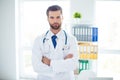 Portrait of serious strict doctor in white coat standing with cr