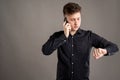 Portrait of serious stylish attractive man dressed with a casual black shirt talking on the phone and looking his watch Royalty Free Stock Photo