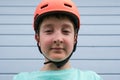 Portrait of a serious teen caucasian boy wearing orange sport crash helmet, learning to ride bicycle or skateboard in