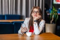 Portrait of serious thoughtful beautiful stylish brunette young woman in glasses sitting, holding her mobile smart phone and Royalty Free Stock Photo