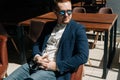 Portrait of serious thoughtful young man in sunglasses wearing stylish suit wear sitting in armchair, looking away out Royalty Free Stock Photo