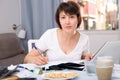 Serious woman with documents using laptop at kitchen table Royalty Free Stock Photo