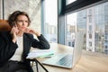 Portrait of serious woman having negotiation over the phone. Businesswoman with smartphone, looking at laptop screen Royalty Free Stock Photo