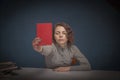 Portrait of serious woman teacher with books pointing red card as symbol of failed exam by a student