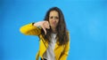Portrait of serious woman in yellow jacket showing thumbs down sign to dislike in Studio with blue Background. Royalty Free Stock Photo
