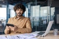 Portrait of a serious and worried young Indian man sitting in the office at a desk, working with documents and at a Royalty Free Stock Photo