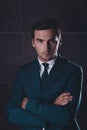 Portrait of serious young businessman in black suit with crosed hands