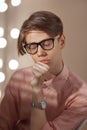 Portrait of puzzled funny young European man wearing glasses, shirt in a strip siting indoors with pensive face and eyes