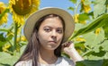 Portrait of a serious young girl of 17-20 years old in a straw hat against a background of blooming sunflowers. Photo shoot agains