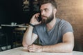 Portrait of serious young handsome bearded hipster man sitting in cafe at table and talking on his cell phone. Royalty Free Stock Photo