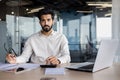 Portrait of a serious young Indian man accountant, financial expert, analyst sitting in the office at a desk with Royalty Free Stock Photo