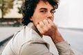 Portrait of serious young man with curly hair looking at the camera, sitting outside. Portrait of handsome male with curly hair Royalty Free Stock Photo