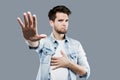 Serious young man makes stop gesture with palm over gray background. Royalty Free Stock Photo