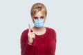 Portrait of serious young woman with surgical medical mask in red blouse standing and looking at camera with warning finger and Royalty Free Stock Photo