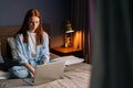 Portrait of serious young woman working typing on keyboard laptop computer sitting in bed at bedroom Royalty Free Stock Photo