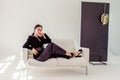 Portrait of a sexy beautiful brunette in a black suit on a white sofa Royalty Free Stock Photo