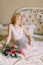 Portrait of blonde bride in white underwear sitting on bed. Bouquet with red roses Royalty Free Stock Photo