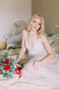 Portrait of blonde bride in white underwear sitting on bed. Bouquet with red roses Royalty Free Stock Photo