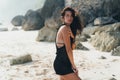 Portrait of brunette model in knitted sweater posing on the sandy beach, big stones and rock on background. Royalty Free Stock Photo