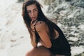 Portrait of brunette model in knitted sweater posing on the sandy beach, big stones and rock on background. Royalty Free Stock Photo