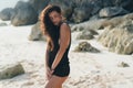 Portrait of brunette model in knitted sweater posing on the sandy beach, big stones and rock on background. Royalty Free Stock Photo