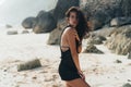 Portrait of brunette model in knitted sweater posing on the sandy beach, big stones and rock on background. Royalty Free Stock Photo