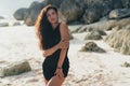 Portrait of brunette model in knitted sweater posing on the sandy beach, big stones and rock on background. Royalty Free Stock Photo