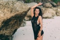 Portrait of brunette model in knitted sweater posing on the sandy beach, big stones and rock on background. Royalty Free Stock Photo