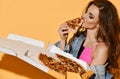 Portrait of sexy brunette woman in pink swimsuit and denim jacket holds a box of fresh tasty pizza eating a slice Royalty Free Stock Photo