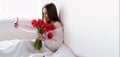 Portrait of a sexy girl with a bouquet of red tulips in the morning in the bedroom for Valentine& x27;s Day makes a selfie on Royalty Free Stock Photo