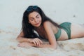 Portrait of sexy girl in green swimwear and sunglasses sits on sandy beach Royalty Free Stock Photo