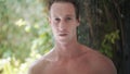 Portrait of sexy man takes refreshing tropical shower, greneery on background