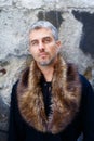 Portrait of a man in wolf fur and thoughtful expression on his face, a structure wall on background