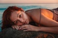 Portrait of a sexy tanned woman in lingerie, posing lying on her stomach, on the coastal rocks. Sea and sunset in the background. Royalty Free Stock Photo