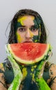 Portrait of a sexy, yellow, green painted woman, facepainting, holding a slice of fresh juicy watermelon in her hand Royalty Free Stock Photo