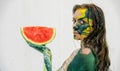 Portrait of a sexy, yellow, green painted woman, like a cat, holding a fresh juicy red watermelon slice in her hand, bodypainting Royalty Free Stock Photo