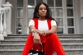 Portrait sexy young African woman with beautiful clean skin in T-shirt in red youth vest with fashionable handbag on street on Royalty Free Stock Photo