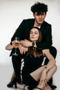 Portrait of sexy young couple in black outfits celebrating holiday with glass of champagne, gray studio background Royalty Free Stock Photo