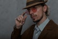 Portrait of a sexy young man in a vintage hat in a stylish jacket in a shirt with a beard on a background of a gray wall indoors. Royalty Free Stock Photo