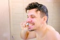 Shaggy sleepy young man intensively cleaning teeth in bathroom, side view.