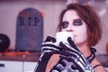 Portrait of shaggy young woman with themed makeup and in skeleton costume, who drinks a hot drink with relaxed and Royalty Free Stock Photo