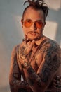 Portrait of a shirtless man with expressive haircut and tattooed body in sunglasses