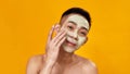 Portrait of shirtless young asian man applying green mask on his face isolated over yellow background. Beauty, skincare Royalty Free Stock Photo