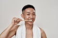 Portrait of shirtless young asian man with problematic skin brushing his teeth with towel around his neck isolated over