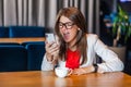 Portrait of shocked, angry beautiful stylish brunette young woman in glasses sitting and looking at her mobile smart phone and Royalty Free Stock Photo