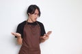 Portrait of shocked Asian barista man in brown apron looking at his mobile phone with surprised expression. Advertising concept. Royalty Free Stock Photo