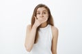 Portrait of shocked attractive girlfriend in white tank-top, covering mouth with palm and staring shocked at camera